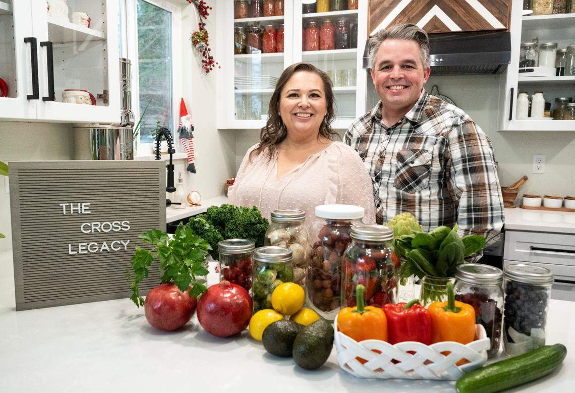 Amy Cross, founder of The Cross Legacy, poses for a portrait with her husband, Michel Cross, and some produce that she has preserved for over three weeks at her home in Bonney Lake, Wash. on Dec. 7, 2022. Amy has amassed over 140,000 followers over the course of a year from sharing tips on social media platforms and her blog about how to preserve food and fresh produce to save money on groceries.