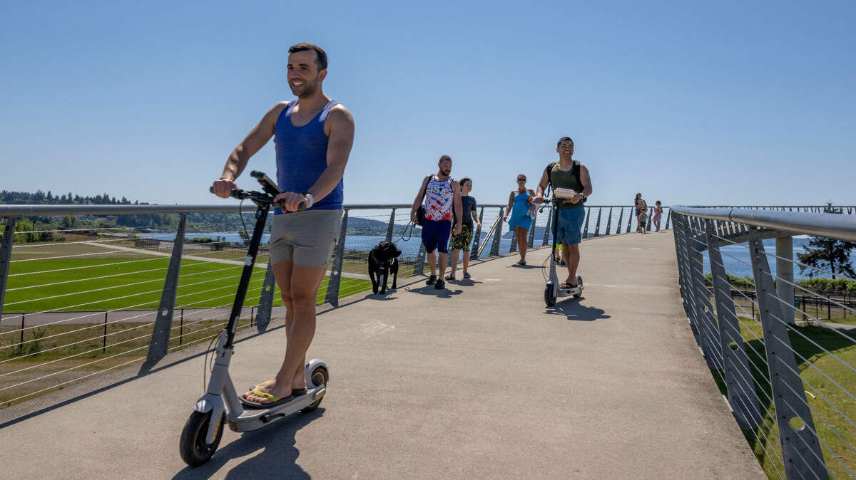 People ride scooters and walk across the bridge on a sunny day at Chambers Creek Regional Park on Saturday, May 13, 2023, in University Place, Wash.