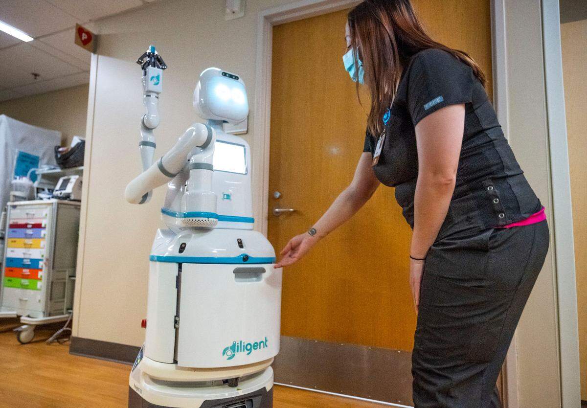 A Tacoma General Hospital registered nurse waits for Moxi, an artificial intelligence (AI) and machine-learning programmed robot, to open its drawer as it delivers medical supplies in the hospital on May 18, 2023.