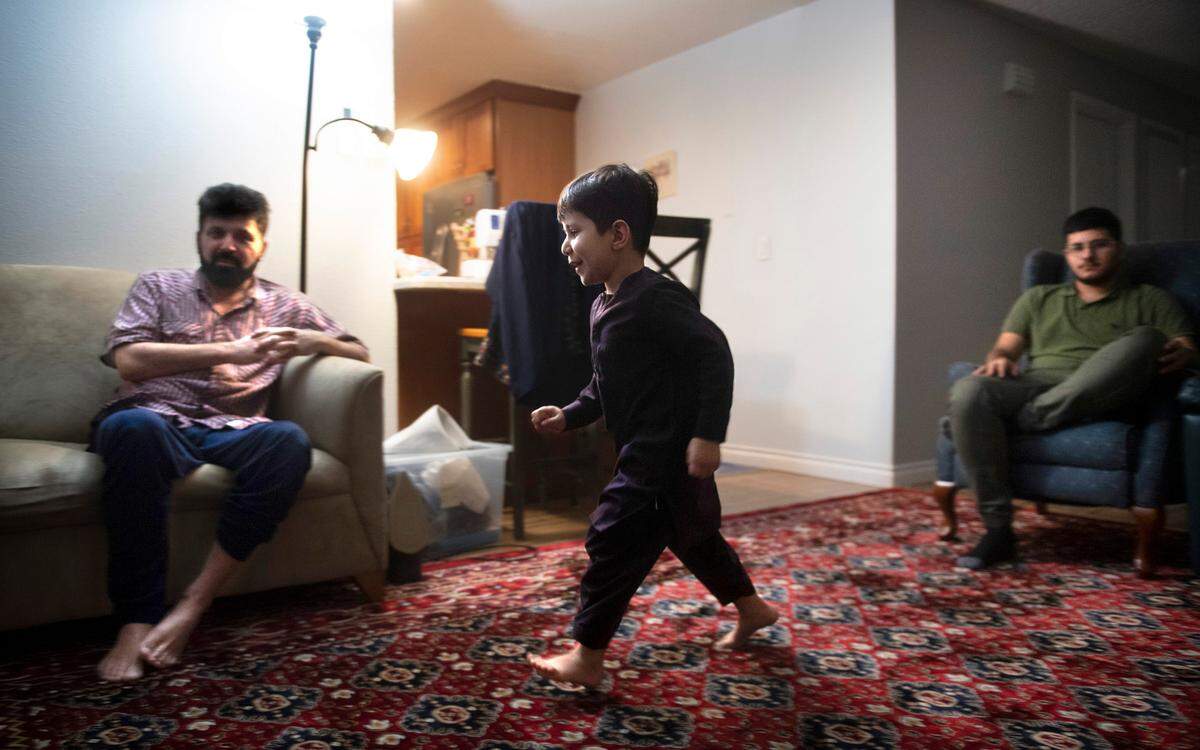 Taha Stanakzai, 4, hustles across the living room as his father, Najibullah Stanakzai, and older brother, Pazhwak, 19, relax at their home in Puyallup, Washington, on Saturday, Feb. 5, 2022.