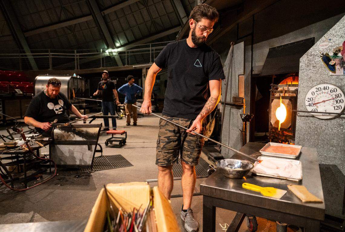 Museum of Glass hot shop director and lead gaffer Benjamin Cobb places a hot piece of glass in colored sand to make it pink while working in the hot shop at the museum in Tacoma, Wash. on Nov. 10, 2022.