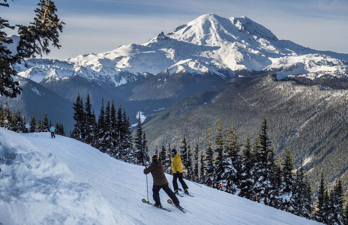 Skiers glide down a route with a full view of Mount Rainier in the distance.