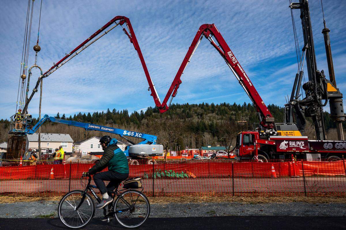 A cyclist rides by along the Foothills Trail as construction continues on an emergency foot bridge in Orting, Wash., on Wednesday, Feb. 26, 2025. The bridge is the first of two planned projects allowing residents to find higher ground in case of a flood or lahar.