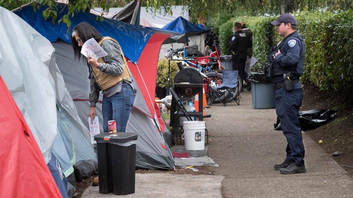 Laurel Howard of Neighborhood and Community Services checks with residents as Tacoma police officer M. Asarim escorts her at the homeless encampment along M Street near The Evergreen State College’s Tacoma campus, in Tacoma, Washington, on Tuesday, Oct. 12, 2021.