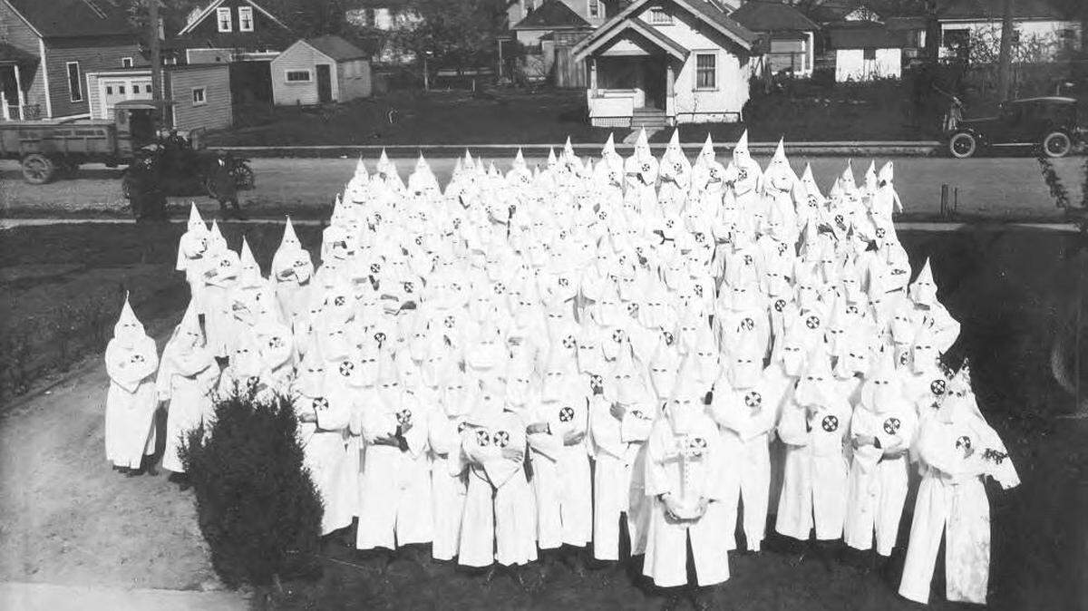According to Tacoma Public Library archives, this photograph of a gathering of the Ku Klux Klan in South Tacoma was taken in April of 1924. The Klan members had gathered behind the Piper Funeral Home at 5436 South Puget Sound Avenue for the funeral of a Tacoma resident.