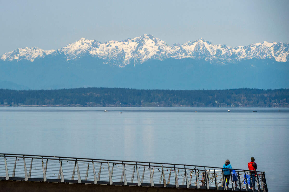 People look over the Puget Sound at the Olympic Mountain range on a Wednesday, April 7, 2022, in University Place, Wash.