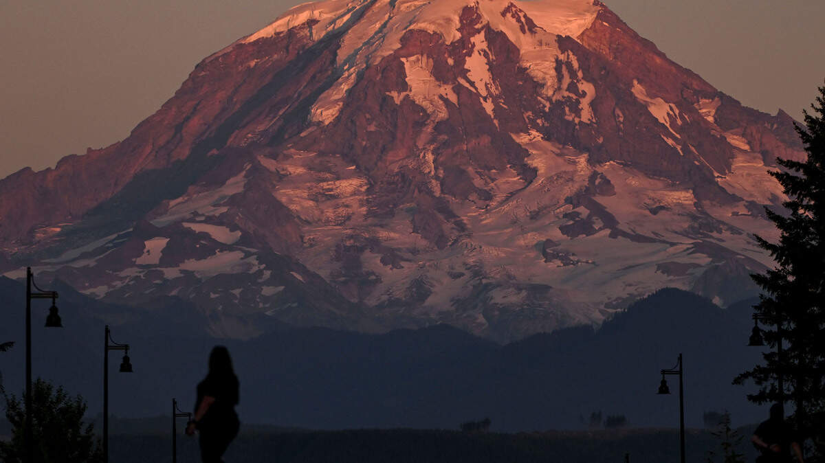 People walk to see the sunset cast pink light on Mount Rainer, Tuesday, Aug. 1, 2023, in Bonney Lake, Wash.