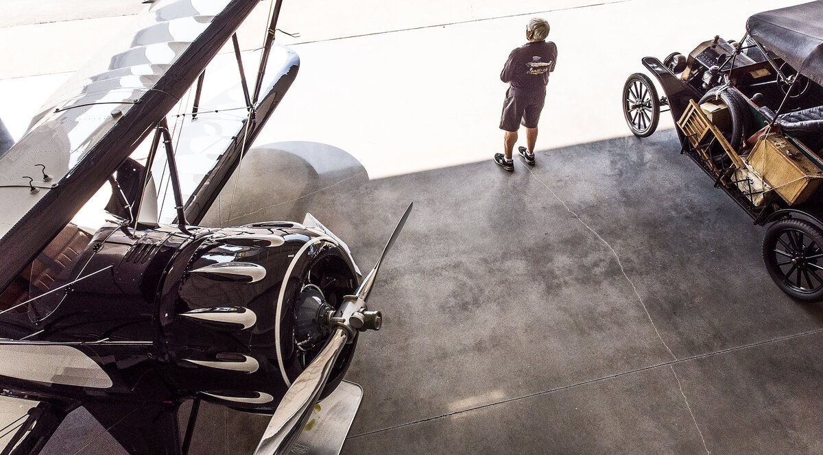 Bob Juranich watches planes take off at Tacoma Narrows Airport in Gig Harbor, Wash., Thursday, Aug. 9, 2018, from his hangar. Juranich is flanked by two of the machines on display in his hanger: a 1934 Waco, left, and a 1914 Ford Model T. Bob Juranich and Bob Johnson built antique planes for the last 30 years. Now, they have 15 of them and counting. Their work are on display in the Point Fosdick Antique Airplane Hangar at the Tacoma Narrows Airport in Gig Harbor, Wash.