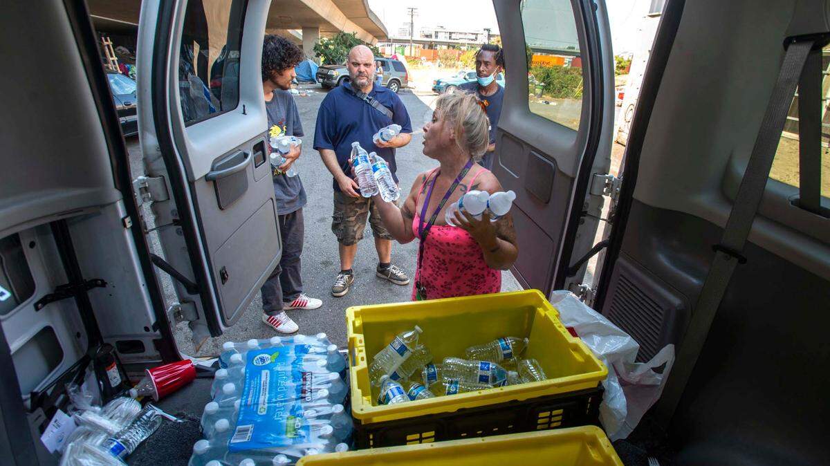 On a sweltering afternoon in August 2021, Traci Abbott of the nonprofit The RISE Center hands out water to people experiencing homelessness in an encampment underneath state Route 509. Pierce County hopes lessons learned during that heat event will better prepare it for the next one.