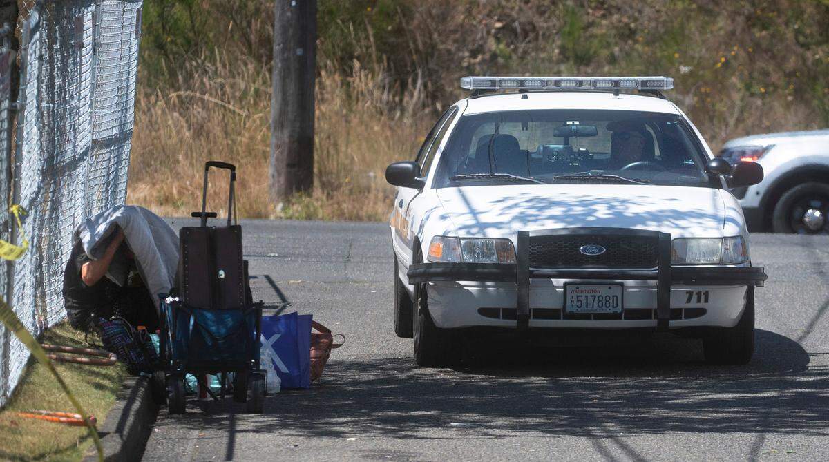 A Tacoma police officer stops in front of a man smoking under a blanket on 84th Street during a visiblity sweep through the Hosmer area in Tacoma, Washington on July 19, 2022. Police Chief Avery Moore told business owners the sweeps are meant for visibilty to reduce illegal activity, and are not for actively confronting crime.