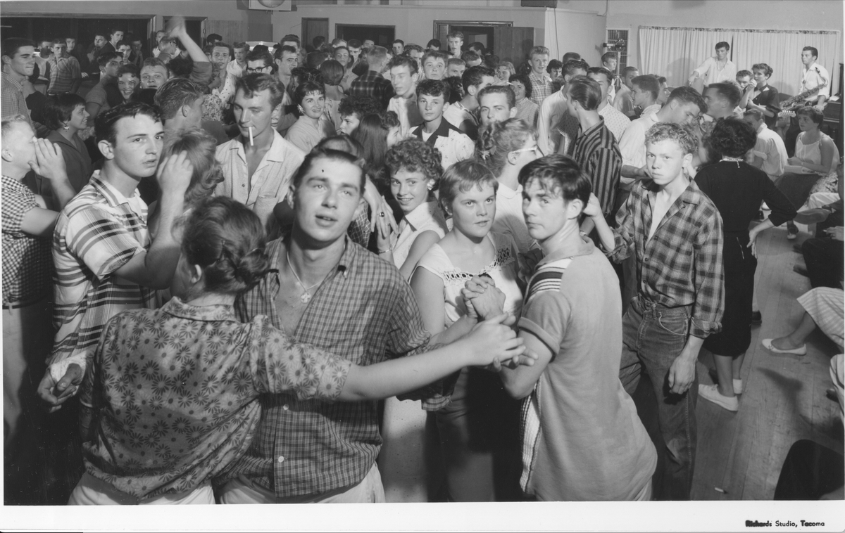 Teenagers packed the Little J.E.M. Dining & Dancing Cafe on July 16, 1958, to rock n’ roll to the music of the Bluenotes. The Little J.E.M. was on Hwy 99 just past the Puyallup River bridge. Set up on a small stage at one end of the room (right corner), the band’s singer, a teenage Rockin’ Robin Roberts, was backed by Lassie Aanes on drums, Bill Engelhart on electric guitar, Buck Ormsby on bass and Frank Dutra on saxophone. The boys were young teens, and one of the first rock ‘ roll bands in the area. In 1958, Duane Eddy released “Rebel Rouser,” Jerry Lee Lewis was “Breathless,” and the Wailers made their first public appearance at Bellarmine High School.