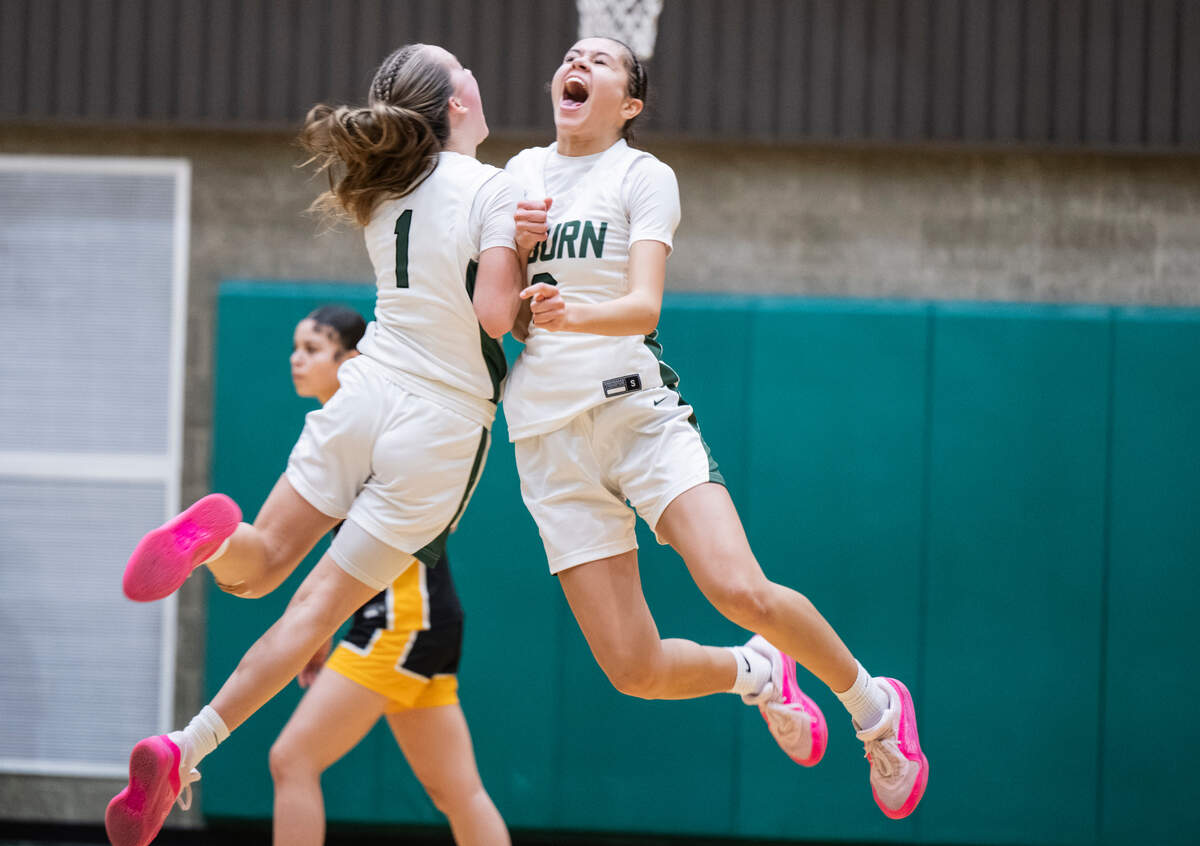 Auburn’s Avery Hansen (1) and Jayla Brown celebrate their 65-53 victory over Lincoln during the opening round of the 3A District 3/4 basketball tournament at Auburn High School on Friday, Feb. 9, 2024, in Auburn, Washington.