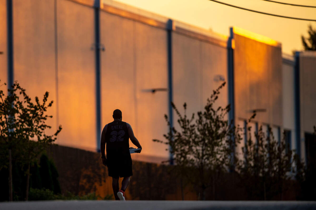 A man walks along 146th Street Southwest past a large Amazon warehouse as the sun sets in Lakewood, Wash., on Thursday, Aug. 18, 2022.