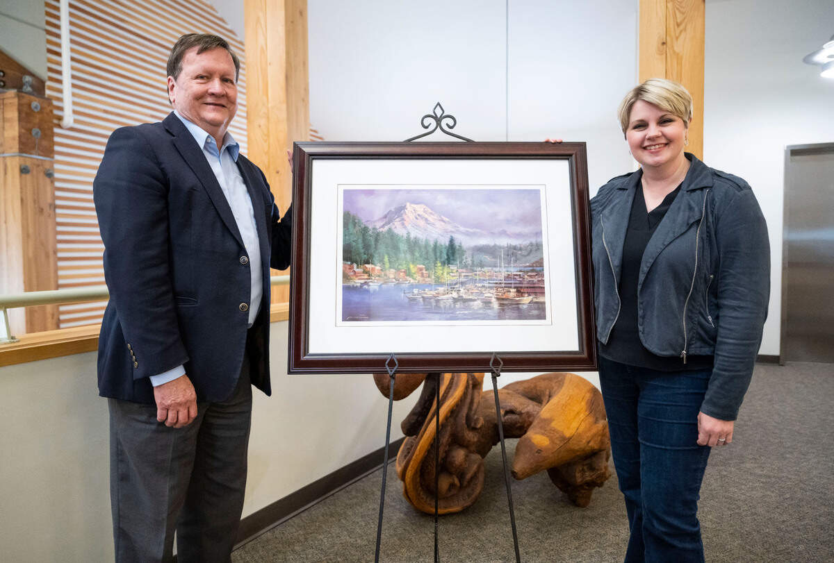 Tim Ham, left, and Mayor of Gig Harbor Tracie Markley, right, pose for a portrait with Afghan artist Abdul’s painting of Gig Harbor that he created while living in hiding with his family from the Taliban in Afghanistan, in Gig Harbor on March 29, 2023.