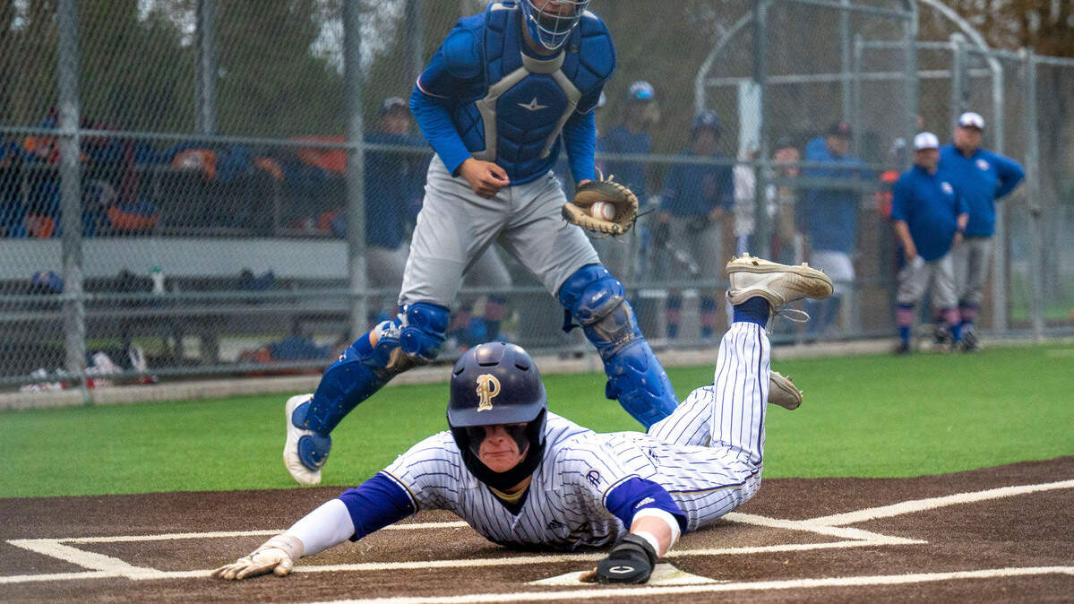 Puyallup’s Garrett Ringer slides safely through home plate as Graham-Kapowsin catcher Brandon Kim looks on after chasing down a wild pitch during a 4A South Puget Sound League game on Tuesday, May 3, 2022, at Heritage Park in Puyallup.