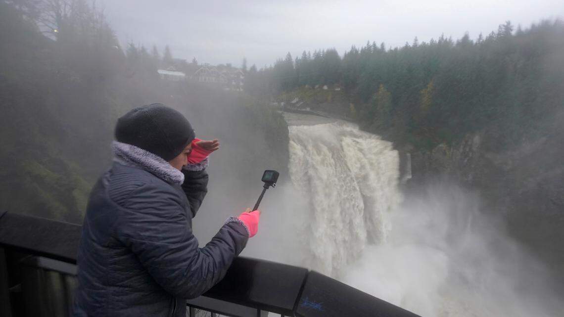 A person records video as water rushes over Snoqualmie Falls, Friday, Nov. 12, 2021, in Snoqualmie, Wash. Forecasters said storms caused by an atmospheric river, known as the Pineapple Express, would cause heavy rain in Oregon and Washington through Friday night. (AP Photo/Ted S. Warren)