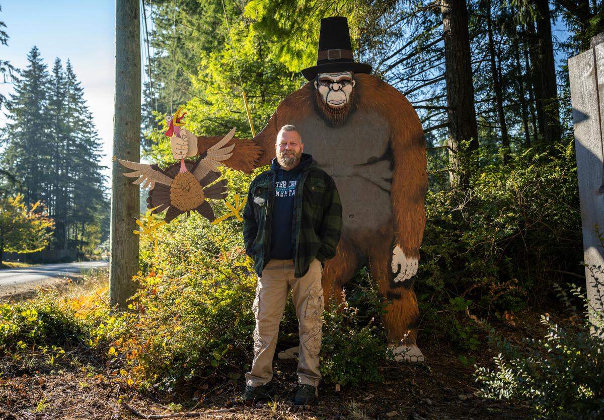 Gig Harbor resident Scott Bows poses for a portrait next to an 8-foot-tall Sasquatch, made of plywood coated in craft paint, that he created with his kids as a weekend project in August. It’s shown standing on the side of the road on Creviston Drive in Gig Harbor, Wash. on Nov. 20, 2022.