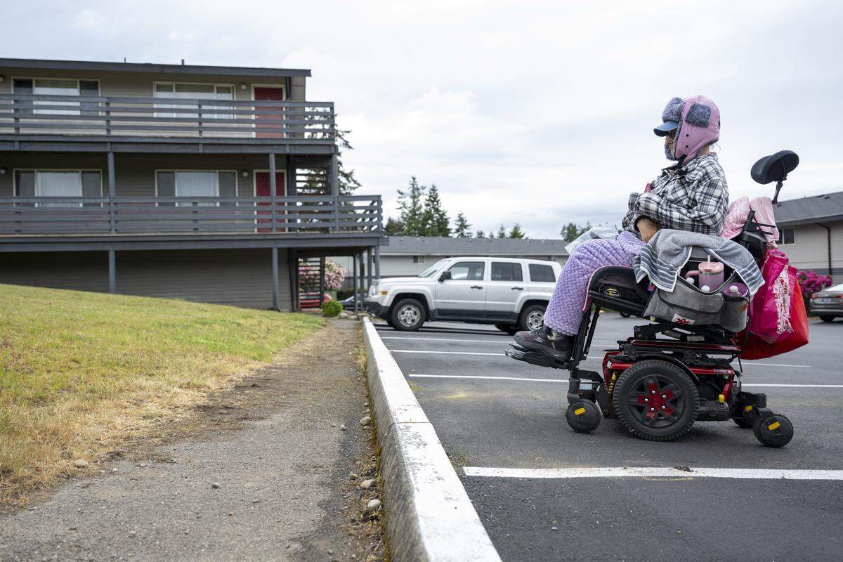 Kimberly Phillips, a resident of Westside Estates, stops her electric wheelchair short of a curb in a parking lot at the apartment complex on Wednesday, May 13, 2026, in Tacoma, Wash. The path is only paved to a certain point, she said, making it muddy and unsuitable to travel when it rains.