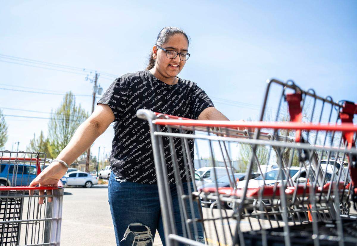 Puyallup High School senior Gurnoor Nagra pushes shopping carts across the Puyallup Food Bank parking lot after delivering meals to families waiting in their cars in Puyallup, Wash. on April 27, 2023. Nagra has been volunteering at the food bank for about two years and has dedicated over 400 volunteer hours to helping her community.