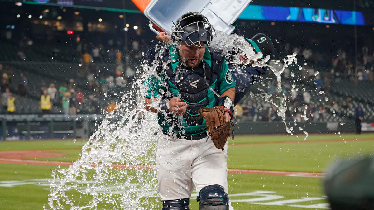 Seattle Mariners catcher Cal Raleigh has water and ice dumped onto him by teammate Tom Murphy as Raleigh takes part in an interview after the Mariners defeated the Oakland Athletics 4-3 in a baseball game Friday, July 23, 2021, in Seattle. (AP Photo/Ted S. Warren)