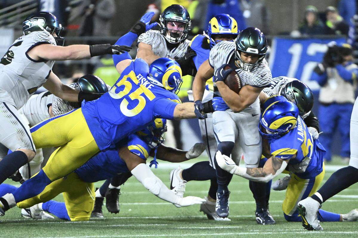 Seattle Seahawks running back Zach Charbonnet (26) carries the ball as Los Angeles Rams defenders close in during the first quarter of the game at Lumen Field, on Thursday, Dec. 18, 2025, in Seattle.