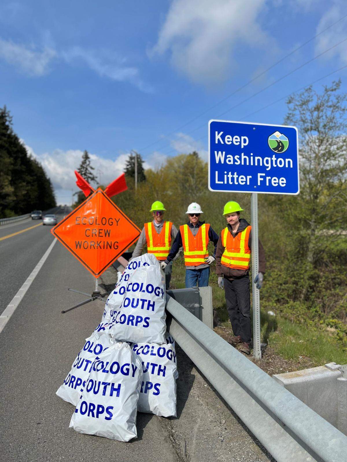 Cleanup crews with the Department of Ecology stand next to bags of collected roadway litter. Every year, the Department of Transportation and DOE spend over $12 million to collect litter.