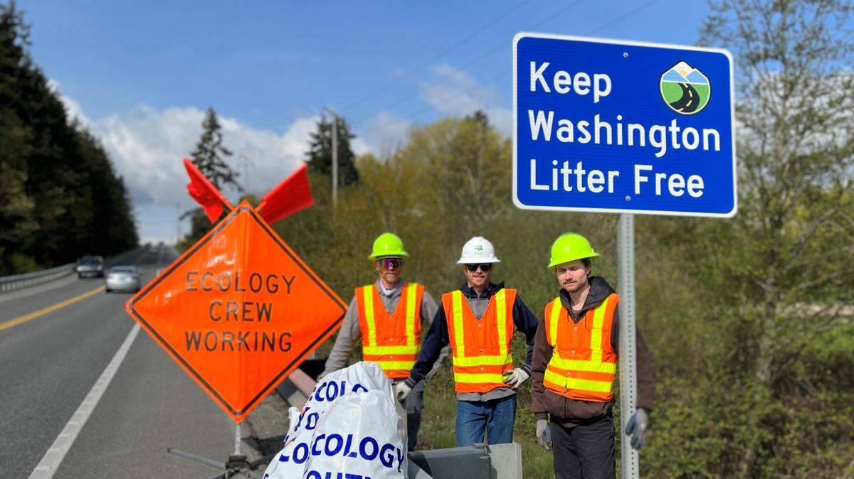 Cleanup crews with the Department of Ecology stand next to bags of collected roadway litter.