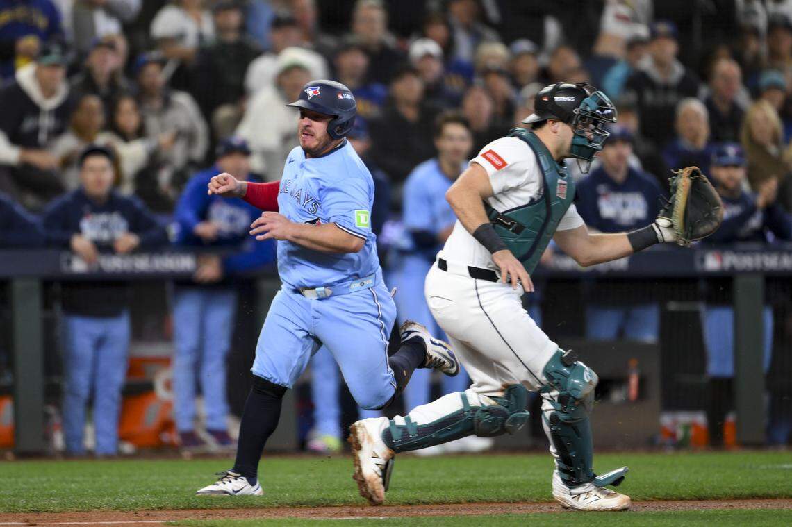 Toronto’s Alejandro Kirk runs past Mariners catcher Cal Raleigh as he scores on a single by Ernie Clement during the sixth inning of Game 5 of the American League Championship Series on Friday, Oct. 17, 2025 at T-Mobile Park in Seattle.
