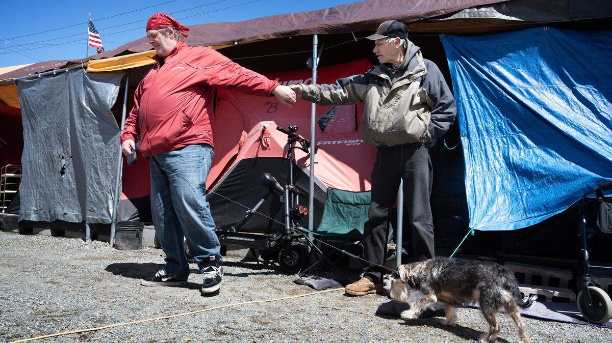 Former residents Jeffery Brown (left) and dog, Peanutbutter Jelly, say goodbye to friend Mark Hurley after stopping by for a social visit at Forward Operating Base Hope veteran’s village in Tacoma on May 29, 2024. The transitional shelter using ice-fishing tents and support services for veterans closed at the end of July. An emergency ordinance that would help FOB Hope find a new site failed in the Pierce County Council meeting July 10, 2024.