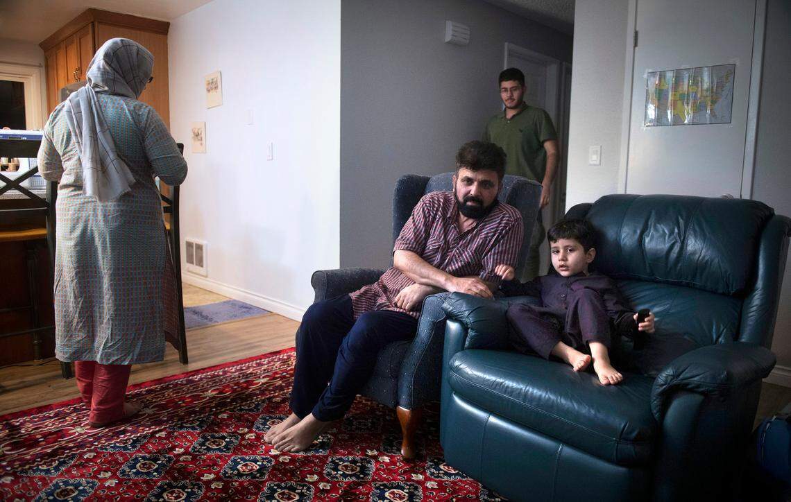 Najibullah Stanakzai sits with is son, Taha, 4, as his wife, Nabila, and son, Pazhwak pass by in the three-bedroom home the family of eight rents in Puyallup, Washington, on Saturday, Feb. 5, 2022.