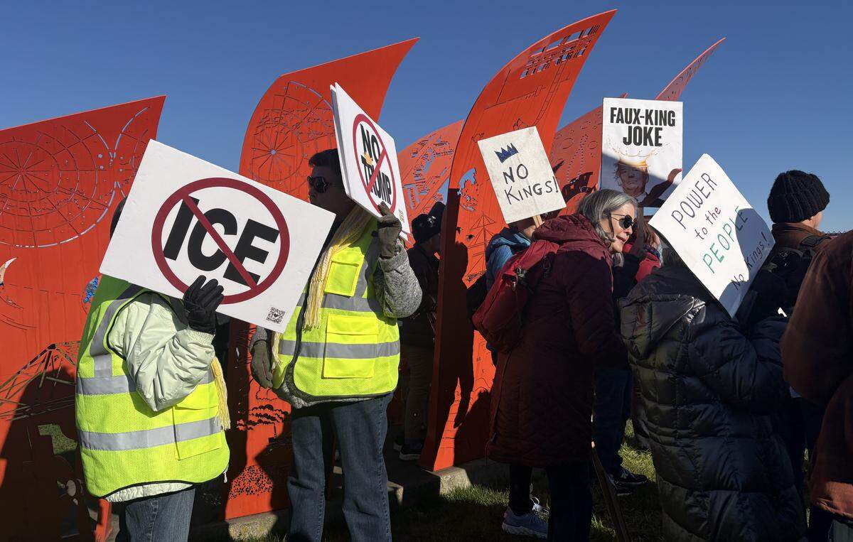 Protestors hold anti-ICE and anti-Trump signs by a sculpture at Fireman’s Park in Tacoma on Saturday, January 24, 2026.