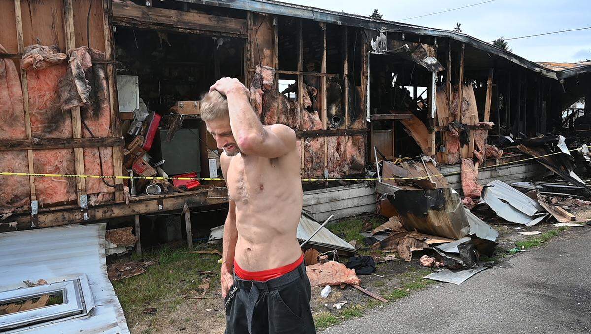 John McLaughlin walks past his next-door neighbor’s trailer that was destroyed by last week’s Lakewood wildfire at the Jamestown Estates mobile home park in Lakewood, Washington, shown on Wednesday, Aug. 9, 2023. McLaughlin used a garden hose to fight off the flames and save his home.