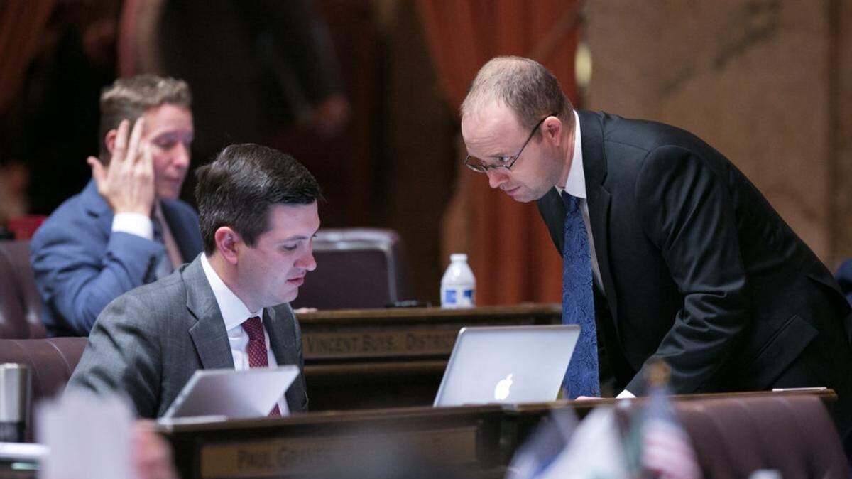 Washington state Reps. Drew Stokesbary (center) and Morgan Irwin (right) have a conversation on the House floor at the state Capitol in Olympia.