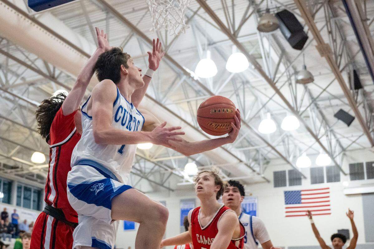 Curtis guard Tyce Paulsen (1) goes up for a reverse lay-in as Camas guard Theo McMillan (20) defends during the first quarter of a District 3/4 semifinal game on Thursday, Feb. 16, 2023, at Curtis High School in University Place, Wash.