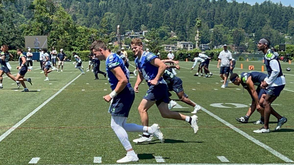 Sam Darnold (14, center facing camera) talks to backup Drew Lock (2, left) as the quarterbacks go through warm-up drills at the first practice of Seattle Seahawks mandatory NFL minicamp June 10, 2025, at the Virginia Mason Athletic Center in Renton.