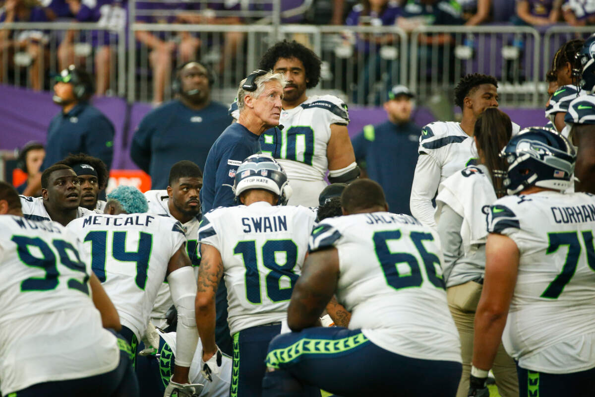 Seattle Seahawks head coach Pete Carroll checks the replay screen as he huddles with his players during an injury time out in the second half of an NFL football game against the Minnesota Vikings in Minneapolis, Sunday, Sept. 26, 2021. (AP Photo/Bruce Kluckhohn)