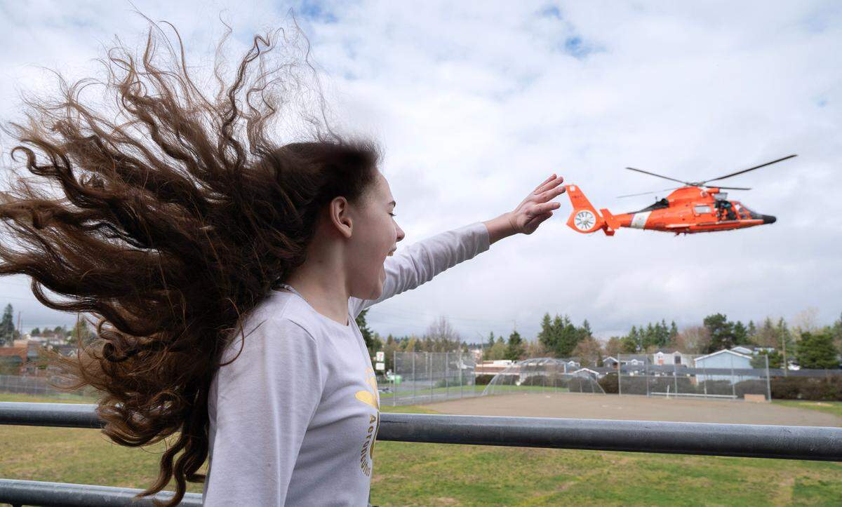 Aeronautics Club member Maci “Goose” Benekas waves to a Coast Guard Dolphin MH-65E rescue helicopter as it arrives for a special visit to Truman Middle School in Tacoma, Washington, on Thursday, Feb. 15, 2023.