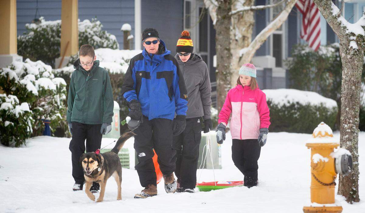 The Coooper family (from left), Minerva the dog, Pardaig, Gareth, Liam and Moira walk home after sledding in the snow in DuPont, Washington, on Tuesday, Dec. 28, 2021.