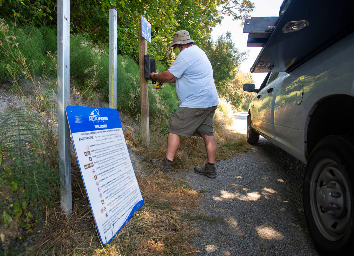 Metro Parks Tacoma gardener Ross Wilton reattaches a bag dispenser for animal waste on Tuesday, July 28, 2020. Vandals recently knocked loose the dispenser, an info sign and tore panels from a mural featuring Native American artwork near the Point Defiance store.