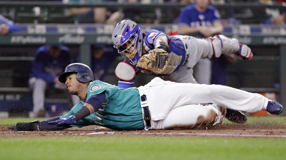 Seattle Mariners’ Jean Segura, bottom, avoids a tag by Texas Rangers catcher Robinson Chirinos while sliding safely home in the second inning of a baseball game Friday, Sept. 28, 2018, in Seattle. (AP Photo/Elaine Thompson)