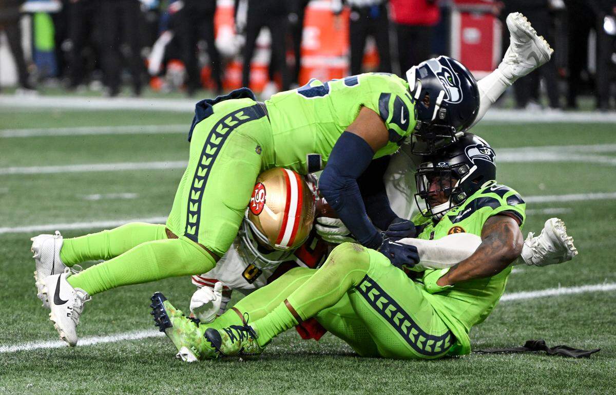 Seattle Seahawks linebacker Jordyn Brooks (56) and safety Quandre Diggs (6) sandwich San Francisco 49ers tight end George Kittle (85) during the third quarter of the game at Lumen Field, Thursday, Nov. 23, 2023, in Seattle, Wash.