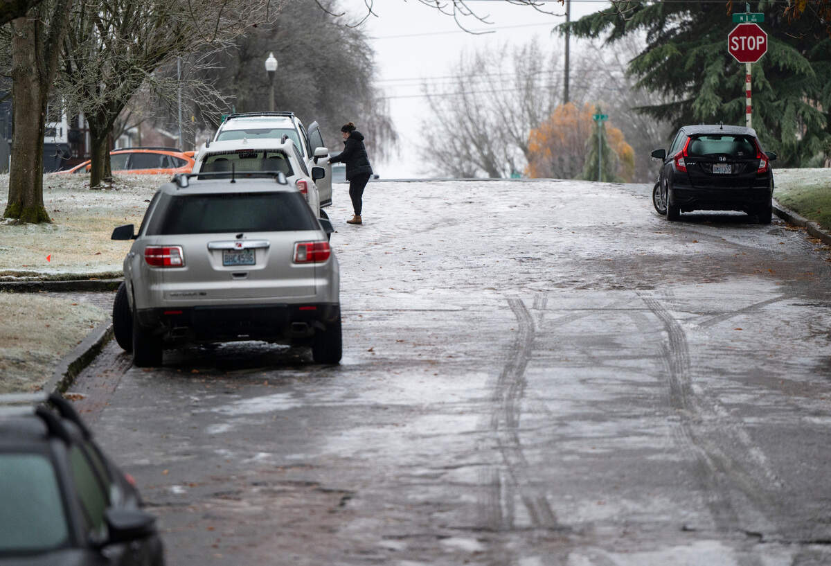 A woman tries to get into her car as she stands on a hill covered in ice after freezing rain left Western Washington under a coating of ice Friday morning in Tacoma, Wash. on Dec. 23, 2022.