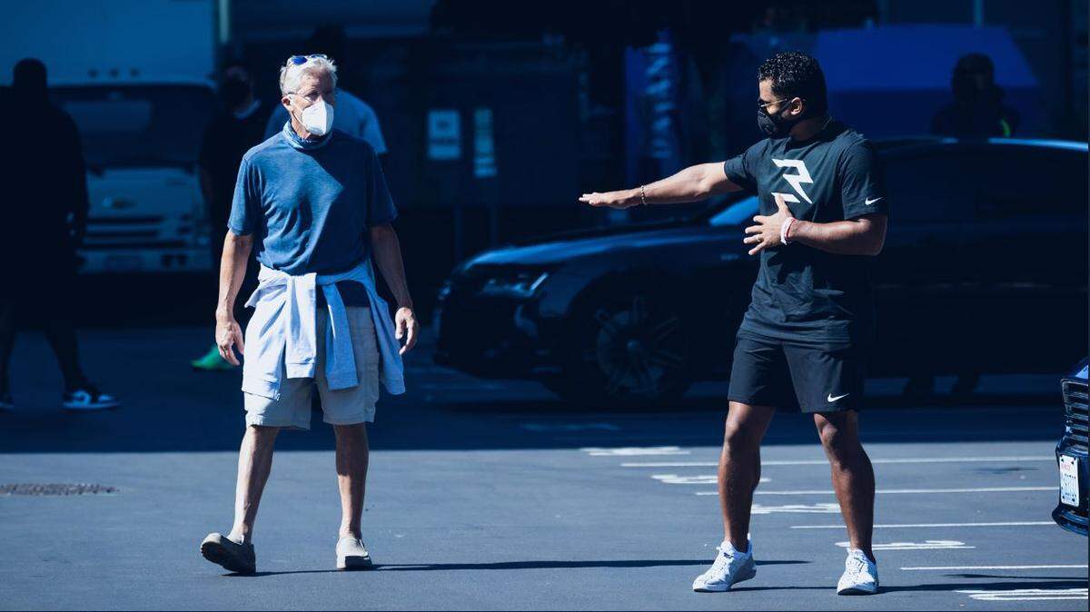 Coach Pete Carroll (left) and quarterback Russell Wilson joke in the players’ and coaches’ parking lot outside the Seahawks’ Virginia Mason Athletic Center in Renton on Tuesday. At least we think they are joking under the masks all team personnel wore to report to training camp. The NFL is requiring masks and COVID-19 tests for three of the next four days before any players can go inside team buildings.