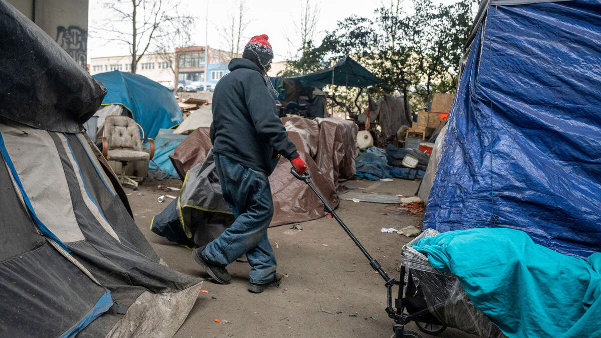 A man pulls a wagon through a maze of Trents and tarps as he helps collect people’s belongings living in the homeless encampment underneath Interstate 705 in downtown Tacoma, Wash., on Friday, Feb. 4, 2022.