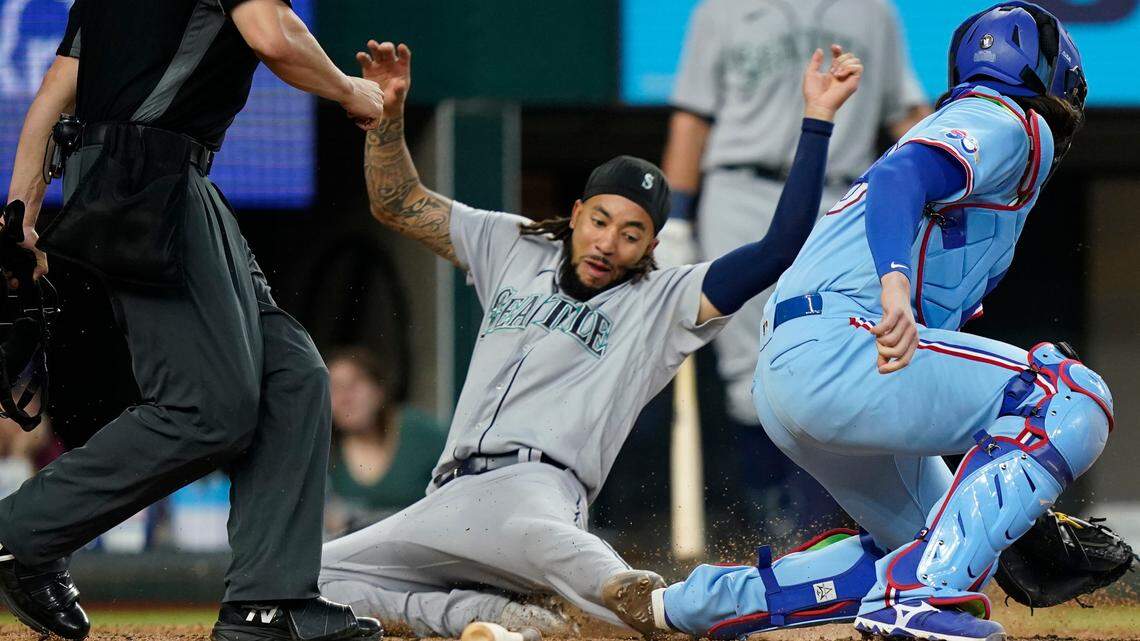 Seattle Mariners’ J.P. Crawford, center, slides into home plate scoring against Texas Rangers catcher Jonah Heim, right, on a double by Mariners’ Eugenio Suarez during the ninth inning of a baseball game in Arlington, Texas, Sunday, June 5, 2022. (AP Photo/LM Otero)