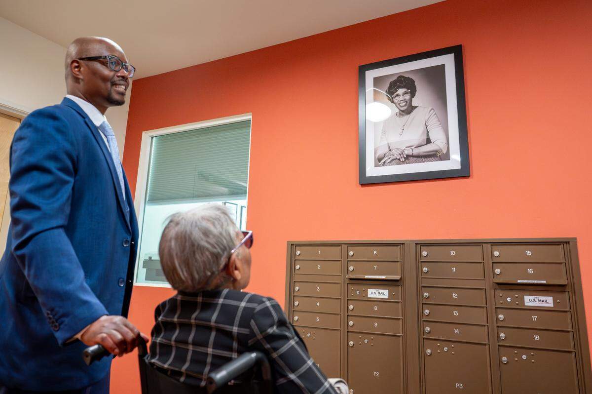 Shiloh Baptist Church Senior Pastor Chavis Young, left, pauses with Maxine Miller, center, to look at a photo of Miller’s mother, Lily V. Brazill, in the lobby of Brazill’s namesake affordable housing complex on Wednesday, May 7, 2025, in Tacoma.