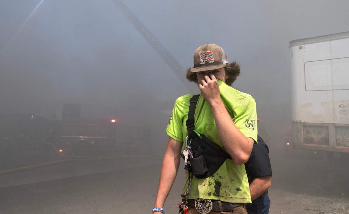 Jacob Pike covers his face as he walks through what Central Pierce Fire and Rescue called toxic smoke as firefighters work on putting out a large debris pile near the 13400 block of Canyon Road E., in Tacoma, Wash., on Friday, June 12, 2024.