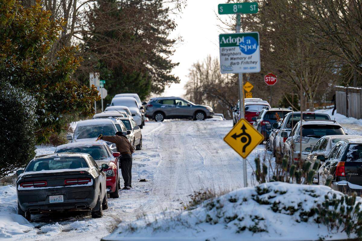 A man cleans the snow off his car parked along an unplowed Ainsworth Avenue while another vehicle drives along Ninth Street in the Hilltop neighborhood in Tacoma on Monday afternoon.