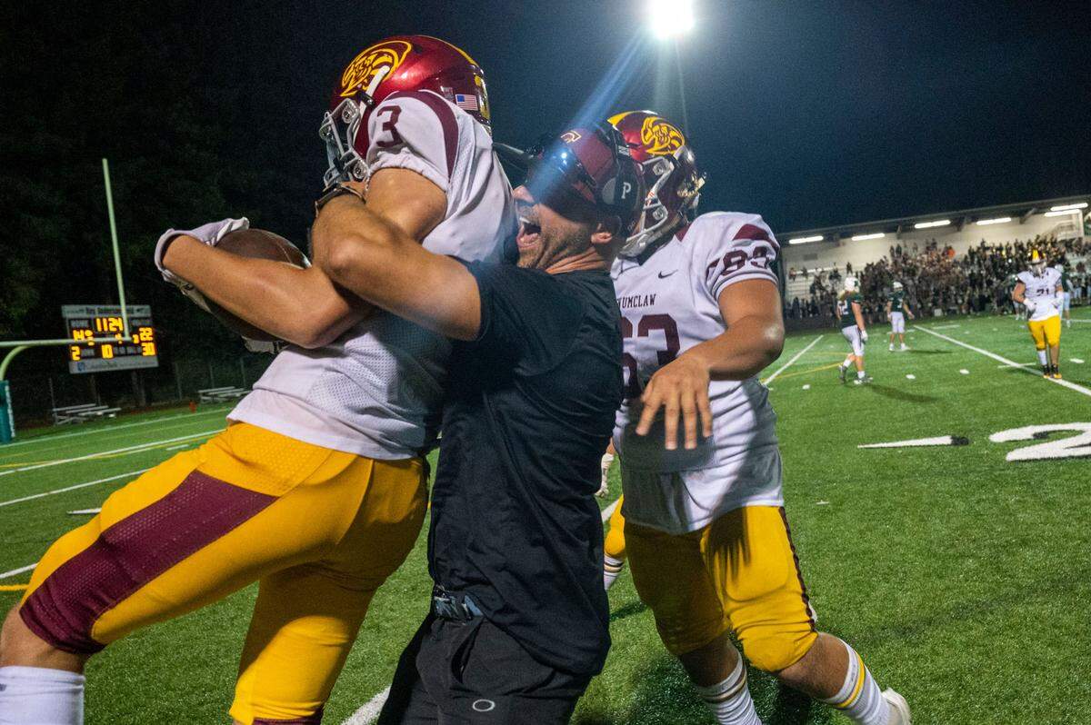 Enumclaw head coach Mark Gunderson hugs defensive back Westin Triplett after his fourth-quarter interception on a pass by Peninsula Payton Knowles during a nonleague game on Thursday, Sept. 1, 2022, at Roy Anderson Field in Gig Harbor Wash.