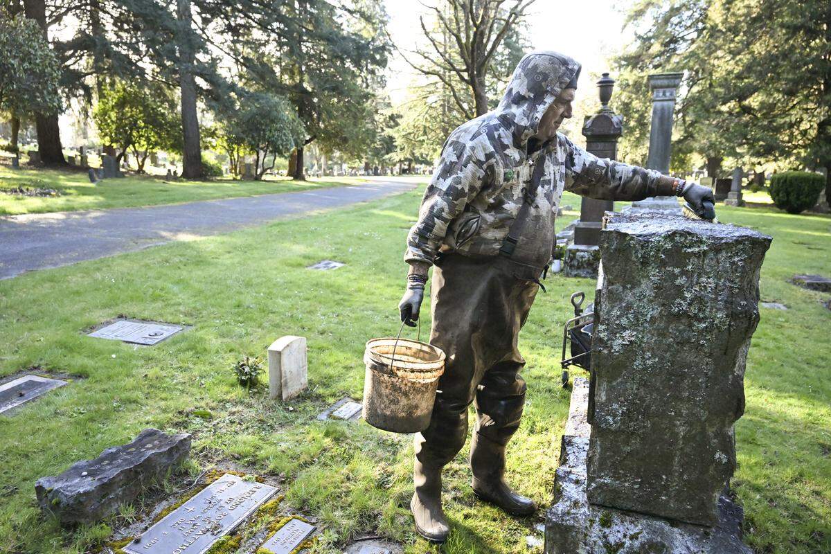 William Fleet scrubs the top of a large headstone at the old Tacoma Cemetery on Monday, March 9, 2026, in Tacoma.